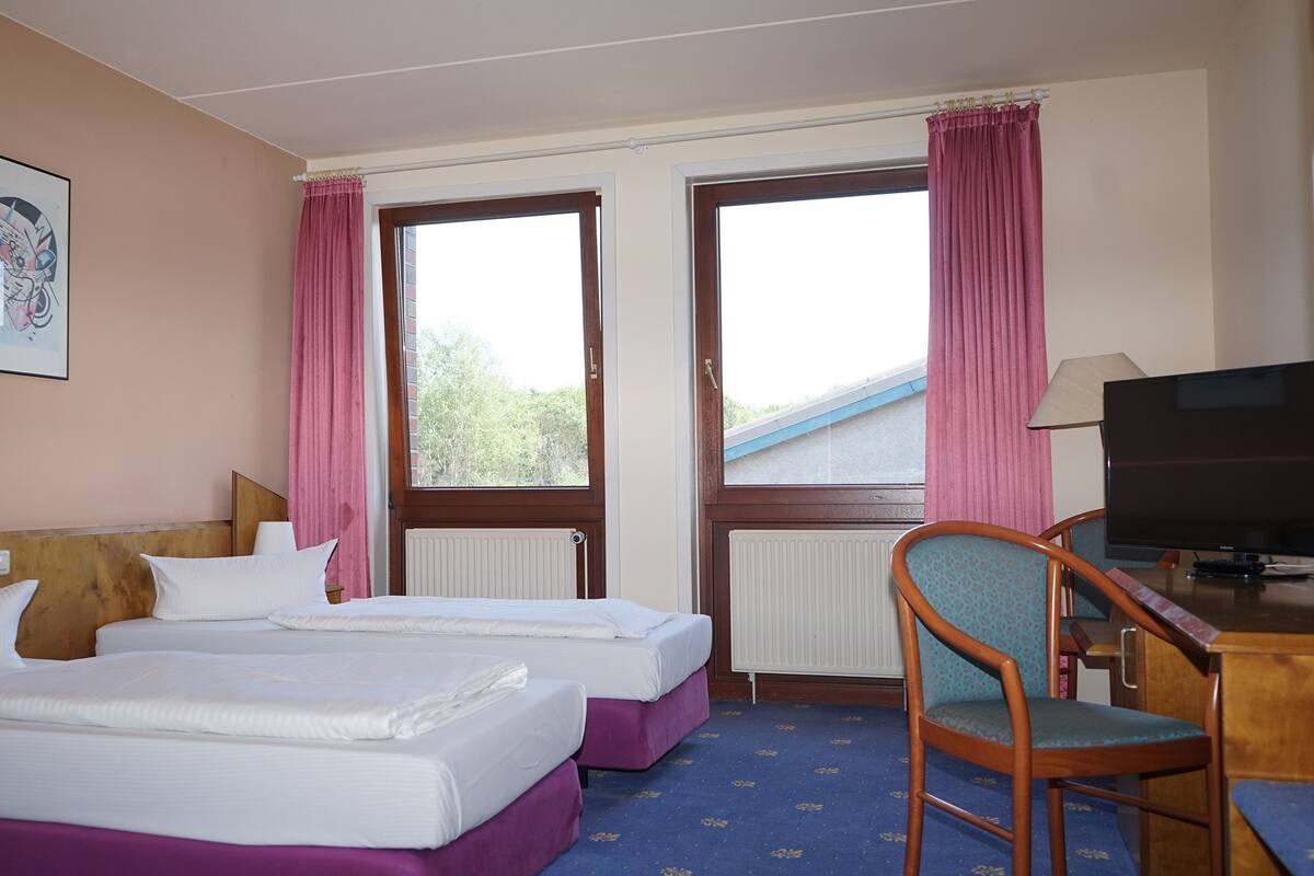 A hotel room with two beds, a television, a desk, and a chair.