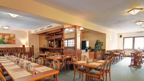 A spacious dining area with multiple tables and chairs, a bar area, and a large window providing natural light. - Entrée Hotel Glinde (Glinde)