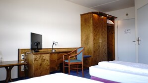 A hotel room with a wooden desk, a chair, a bed, and a wardrobe. - Entrée Hotel Glinde (Glinde)