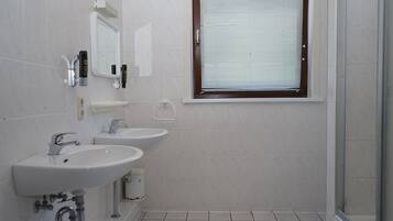 A bathroom with two sinks, a mirror, and a window with blinds.