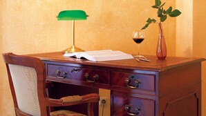 A wooden desk with a green lamp, a vase with a red rose, and a wine glass. - Entrée Hotel Glinde (Glinde)