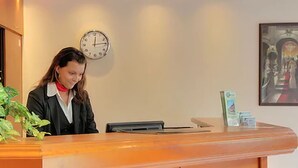 A reception desk with a clock, a framed artwork, and a plant. - Entrée Hotel Glinde (Glinde)
