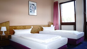 A hotel room with two beds, a wooden headboard, a bedside lamp, a window with a view, and a framed picture on the wall. - Entrée Hotel Glinde (Glinde)