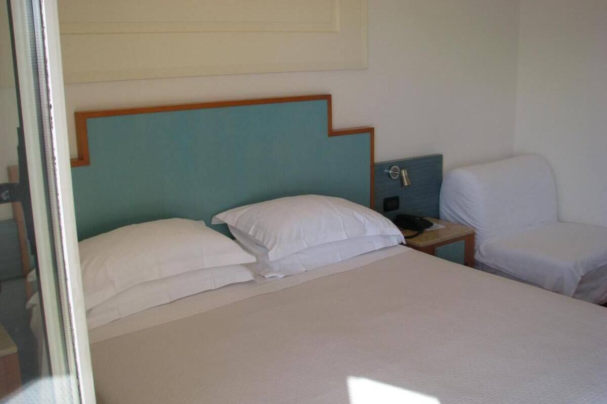 A hotel room with a bed, a nightstand, a chair, and a wall-mounted TV.