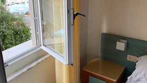 A hotel room with a large window, a small bedside table, a bed, and a headboard. - Hotel Belvedere (Portovenere)