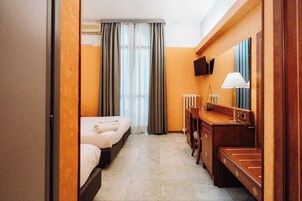 A hotel room with two beds, a desk with a lamp, a television, and a window with curtains.