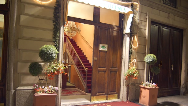 A hotel entrance with a red carpet, a staircase, and two potted plants.