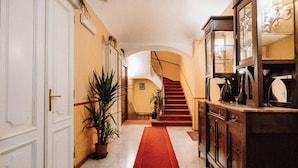 A hallway with a red carpet, a staircase, a wooden cabinet, and a potted plant.