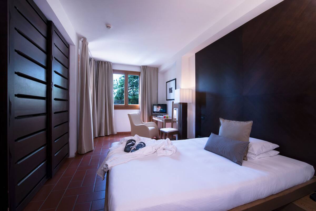Ein Hotelzimmer mit einem großen Bett, einem Schreibtisch mit Computer, einem Sessel und einem Fernseher.