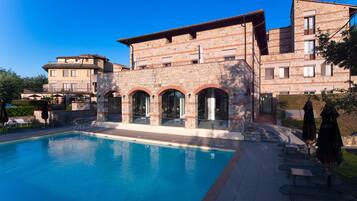 A pool area with a stone building, outdoor seating, and a clear blue sky.