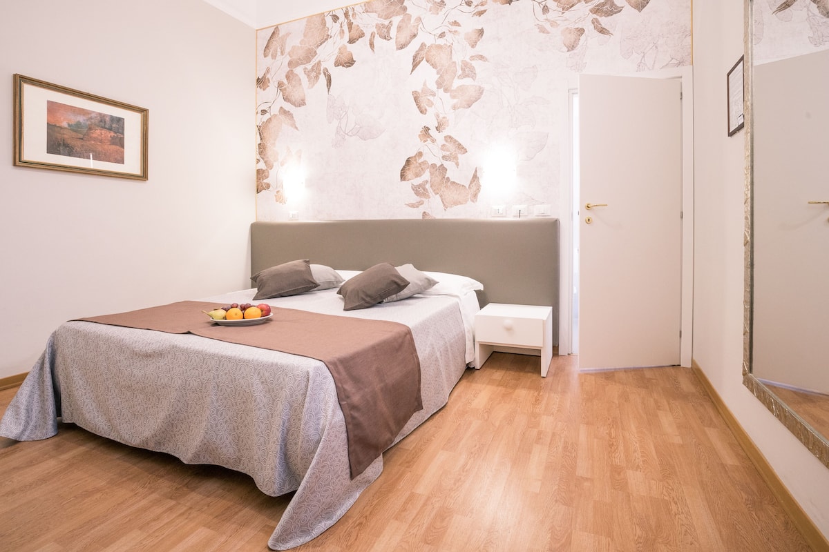 A bedroom with a bed, bedside table, and a fruit bowl on the bed.