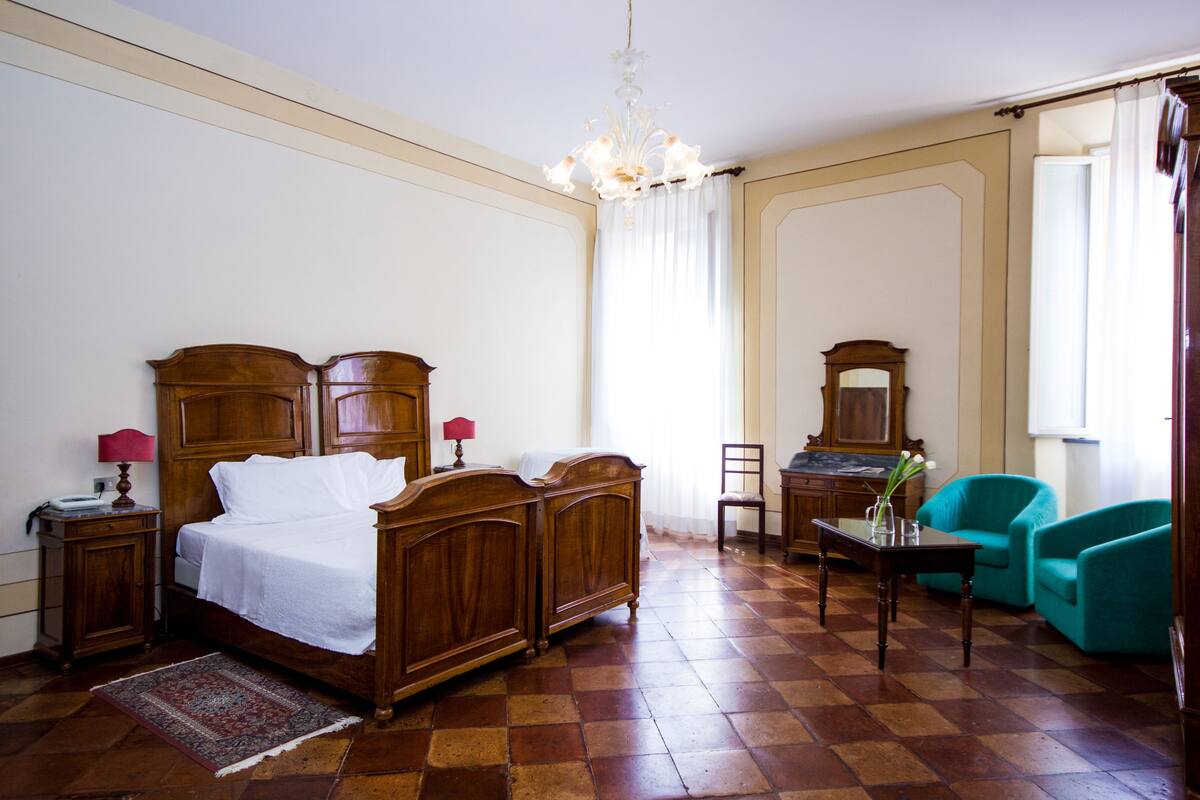 A hotel room with a wooden bed, a desk, a chair, and a teal armchair.