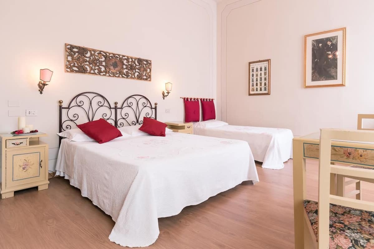 A hotel room with two beds, a wooden floor, a small desk, and a chair.