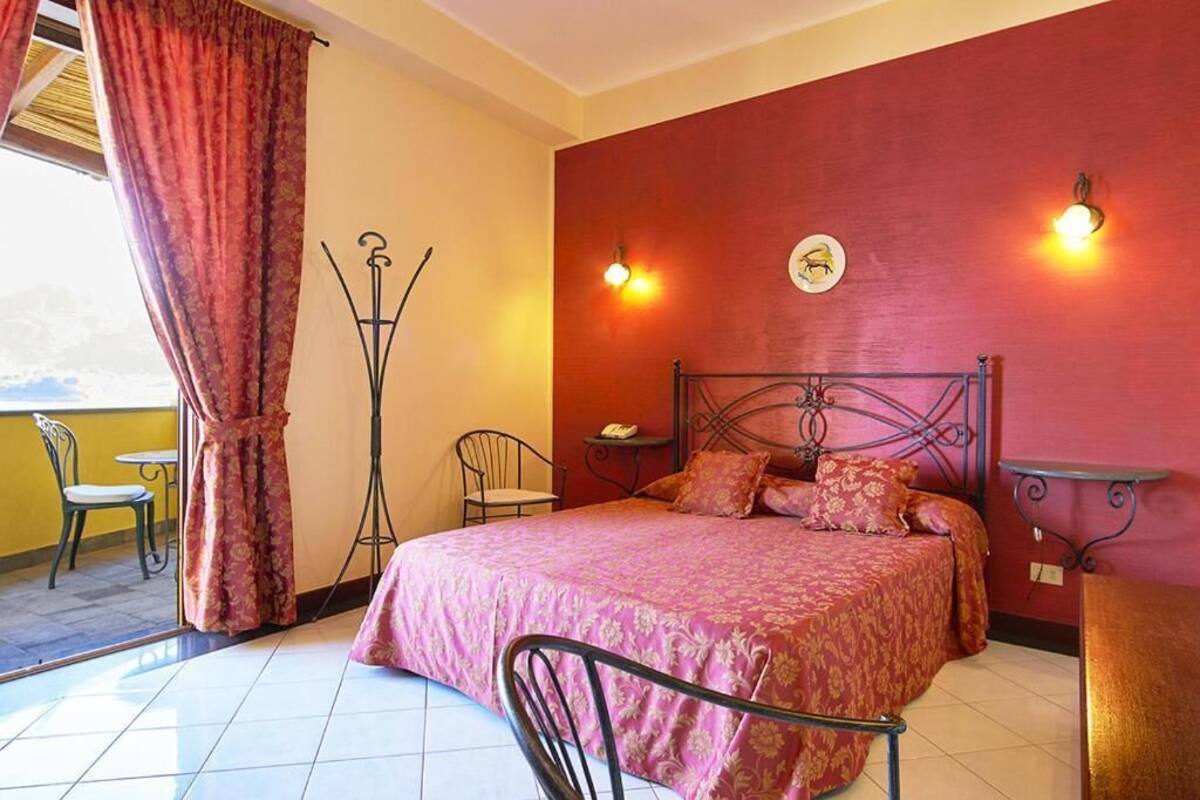 A bedroom with a metal bed frame, a red wall, and a window with curtains.