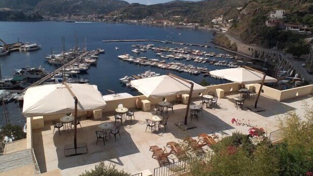 A coastal area with a marina filled with boats, outdoor seating with umbrellas, and a view of the surrounding landscape. - Hotel A' Pinnata (Lipari)