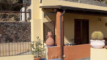 Exterior del Hotel Apinnata, con un muro de piedra, un patio con baldosas y un cactus en maceta.