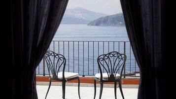 Deux chaises en métal, dotées de coussins, sont placées sur un balcon qui offre une vue sur une étendue d’eau et sur une montagne lointaine.