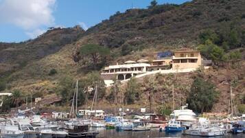 Un port de plaisance avec des bateaux amarrés, un bâtiment portant une enseigne, et un paysage vallonné en arrière-plan.