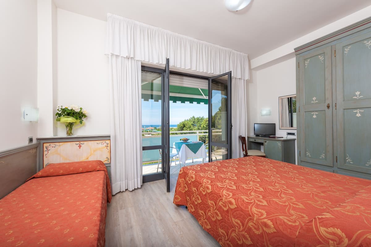 A hotel room with two beds, a TV, a desk, and a view of a pool and greenery.