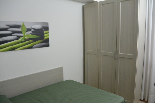 A bedroom with a bed, a wardrobe, and a wall-mounted picture of a plant and stones. - Hotel Suisse (Pietrasanta)