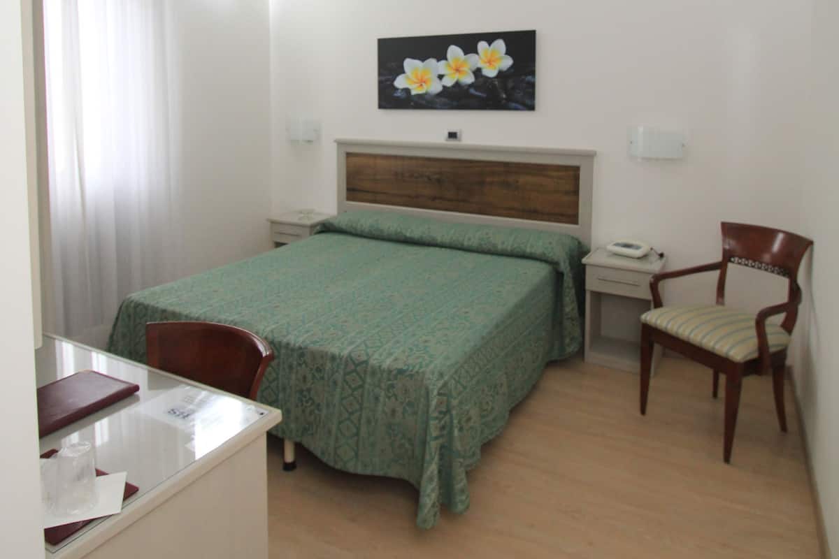 A hotel room with a bed, a desk, a chair, and a nightstand.