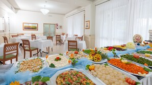 Montaje de bufé en un comedor con varias mesas y sillas, mostrando una variedad de alimentos y una araña.