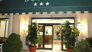 Entrada de un hotel con un letrero que dice "HOTEL SUISSE" y tres estrellas. Hay plantas en macetas frente a la entrada.