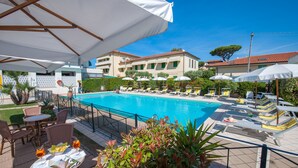 Zona junto a la piscina con sillones de descanso, sombrillas y una piscina.