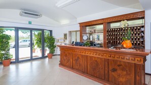 Una zona de recepción con mostrador de madera, plantas en macetas, un espacio para vinos y un ventanal con vistas a la calle.
