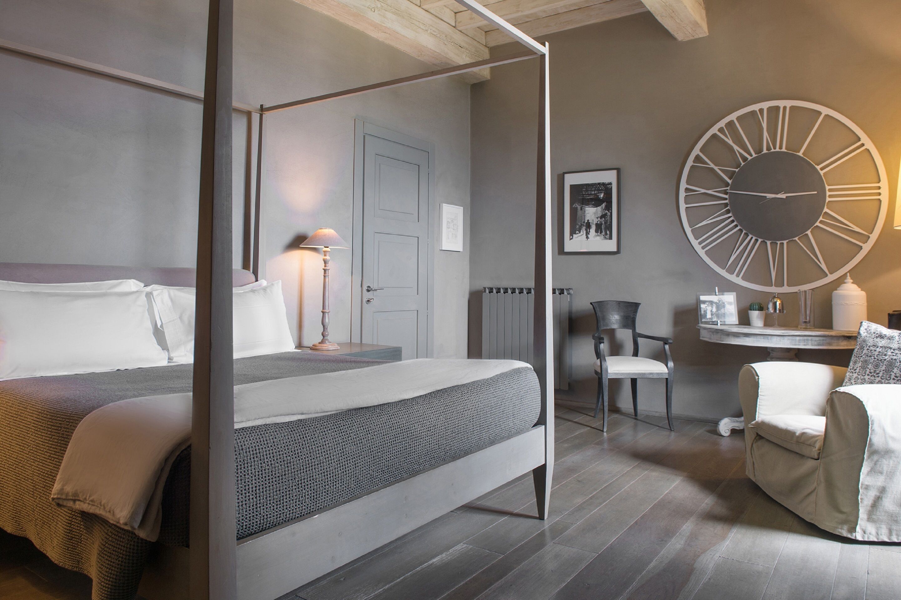 Un dormitorio moderno con cama con dosel, un reloj de pared grande y una zona de estar con una silla y una mesa.