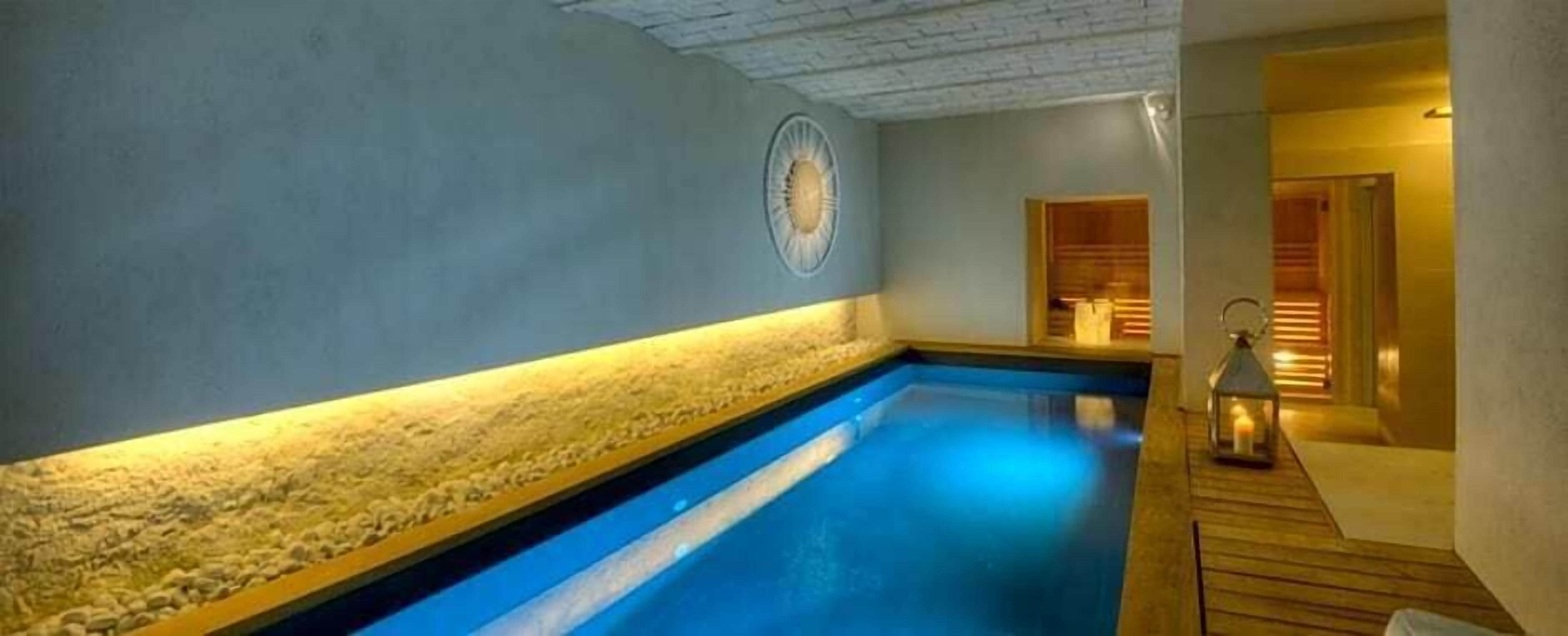 Un'area benessere con piscina blu, una parete in pietra e un pontile in legno.
