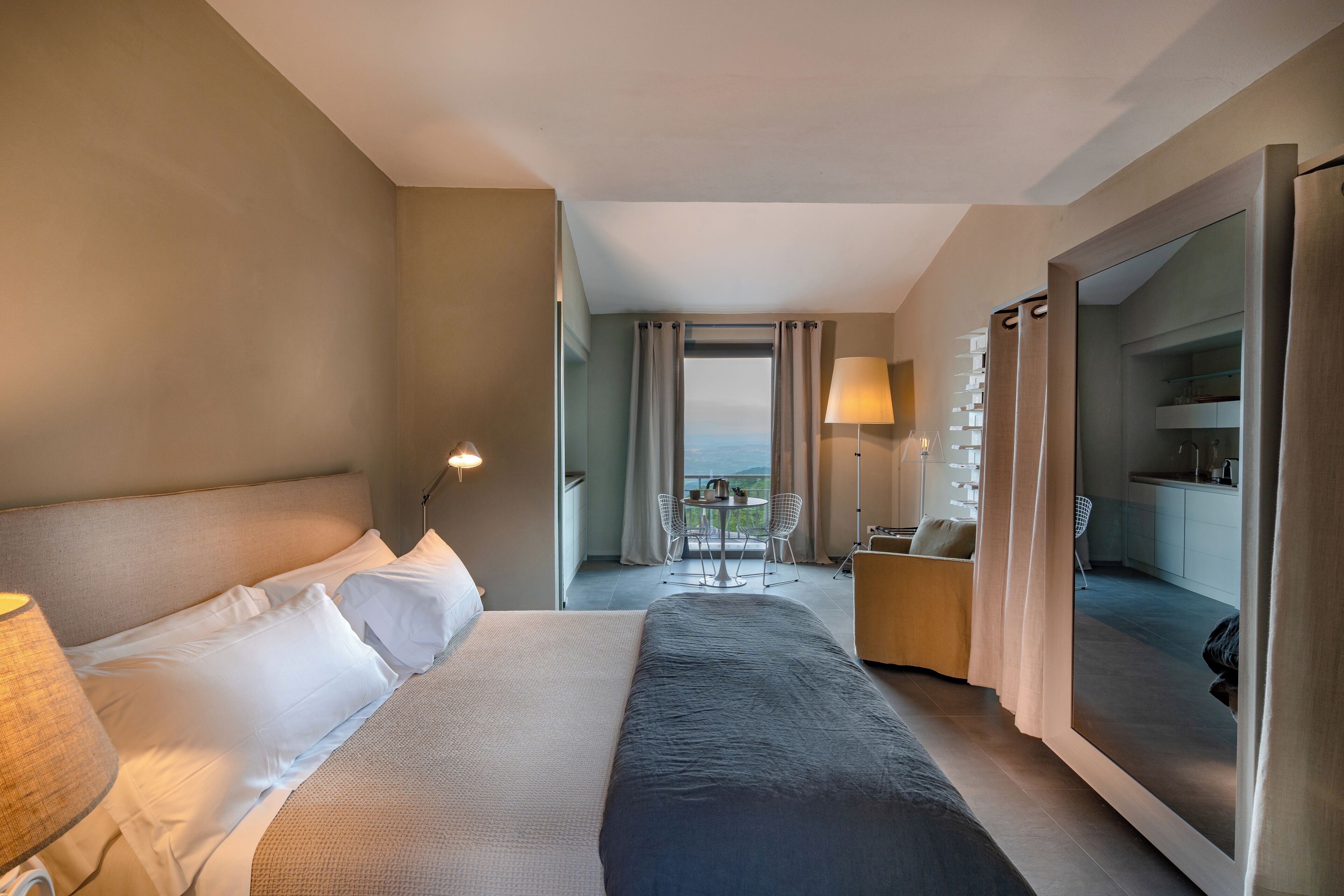 Hotellihuone, jossa on suuri sänky, työpöytä ja tuoli, näkymä ulos ja parveke.