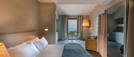 Habitación de hotel con una cama grande, un escritorio con silla, vistas al exterior y un balcón.
