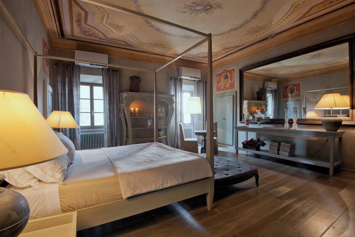 Ein Bett mit Baldachin, ein Nachttisch mit Lampe, ein Stuhl und ein Spiegel über dem Tisch.