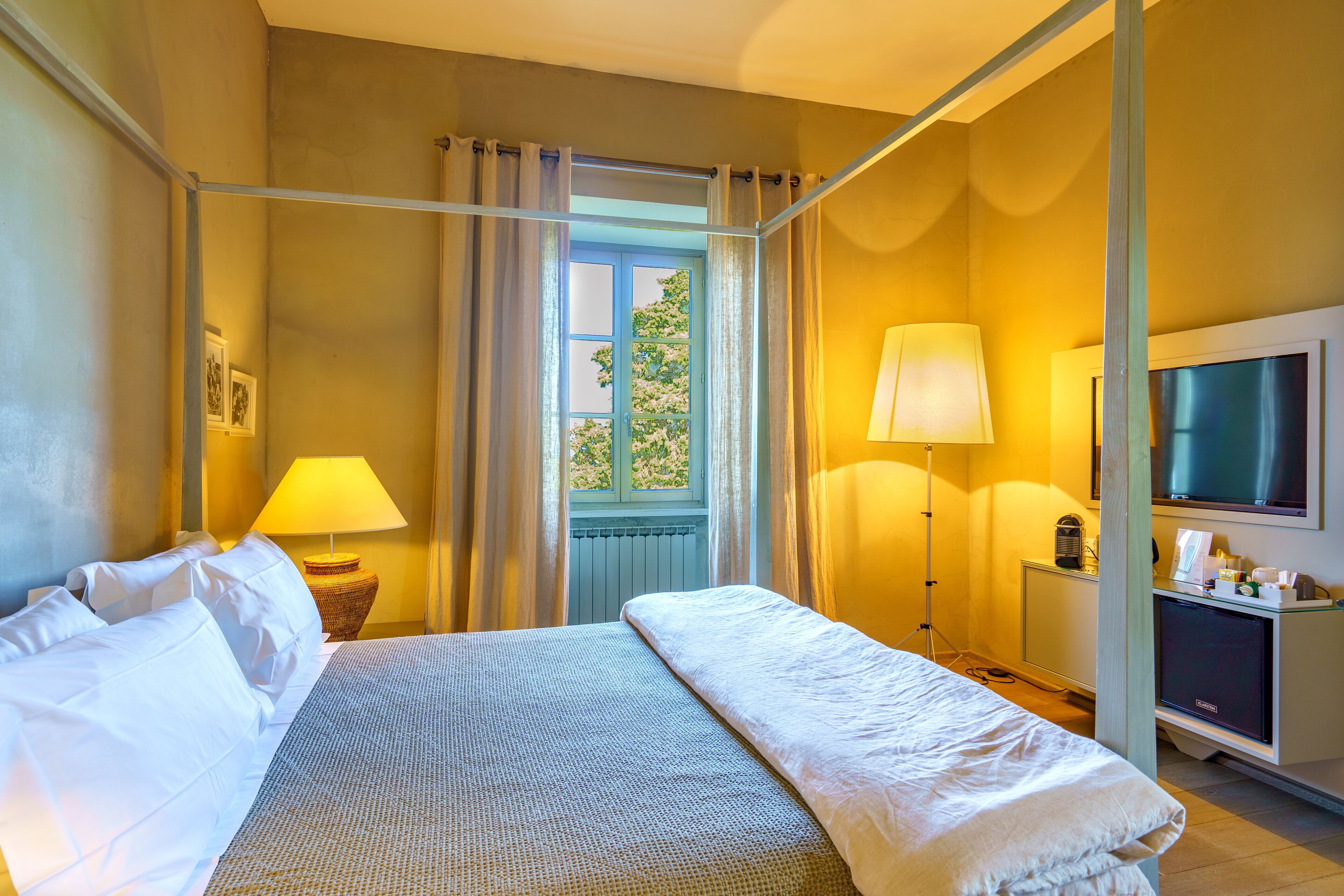A hotel room with a bed, a TV, a lamp, and a window with curtains.