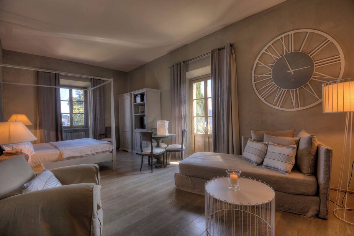 Ein Hotelzimmer mit zwei Betten, einem Schlafsofa, einem kleinen Tisch mit Kerze, einem Schreibtisch mit Stuhl und einer großen Wanduhr.