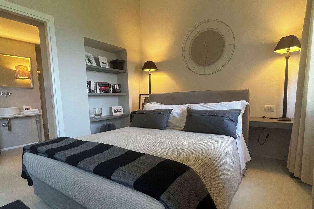 Ein Schlafzimmer mit Bett, Nachttischlampen, einer Wanduhr und einem Regal mit Büchern und Dekoration.