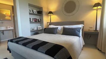 Un dormitorio con cama, lámparas de noche, un reloj en la pared y una estantería con libros y objetos decorativos.