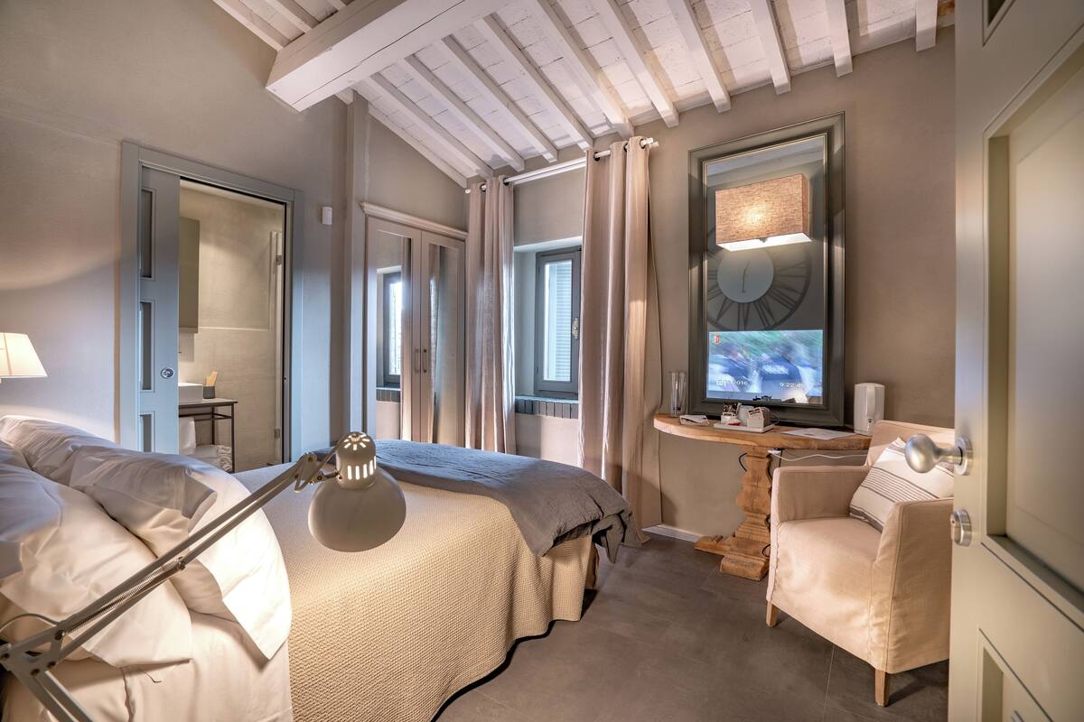 Ein modernes Schlafzimmer mit Bett, Nachttisch, Sessel und Fernseher.