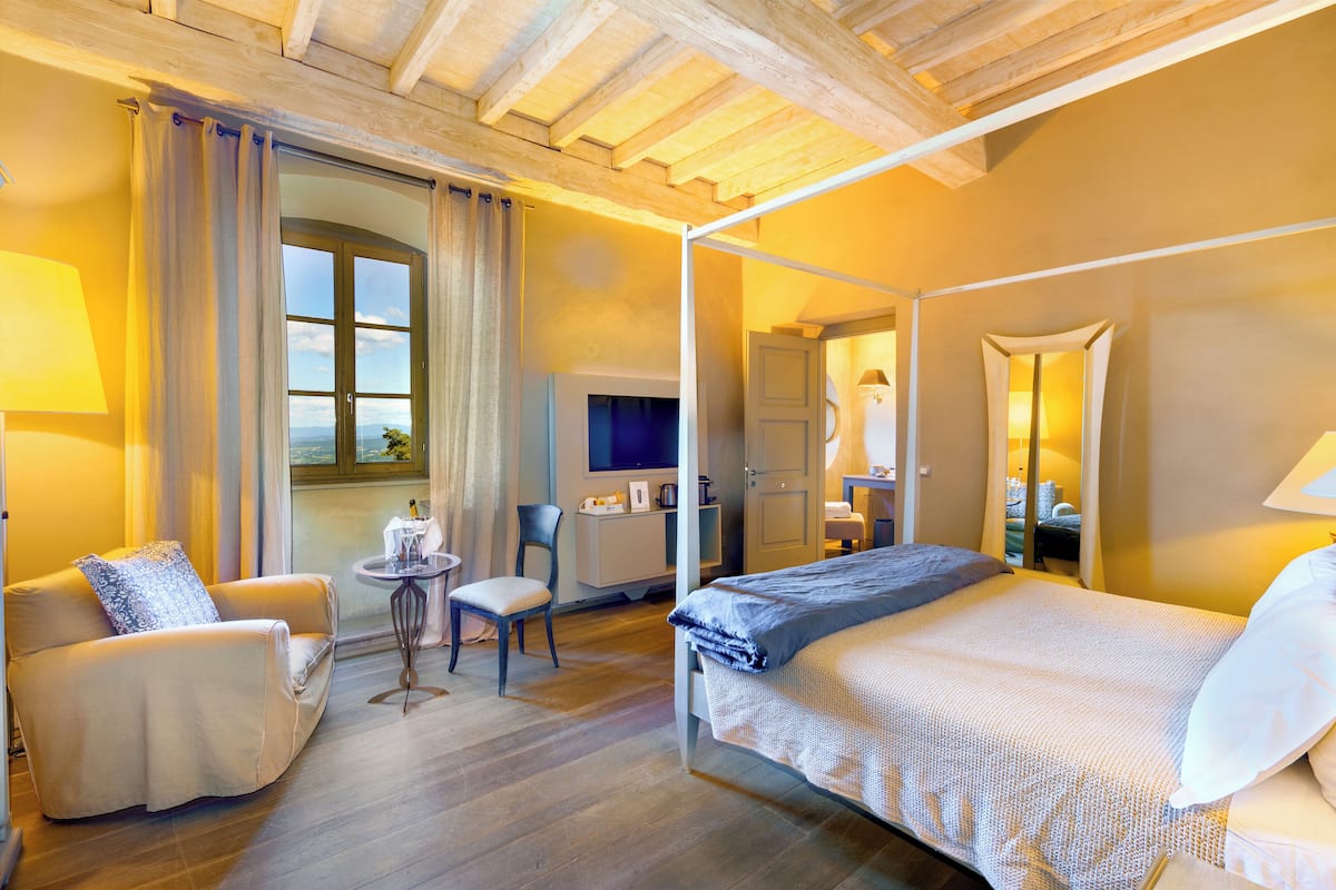 Ein Bett mit Baldachin mit Blick ins Freie, ein Schreibtisch mit Stuhl und eine Couch in einem Zimmer mit Holzbalken an der Decke.