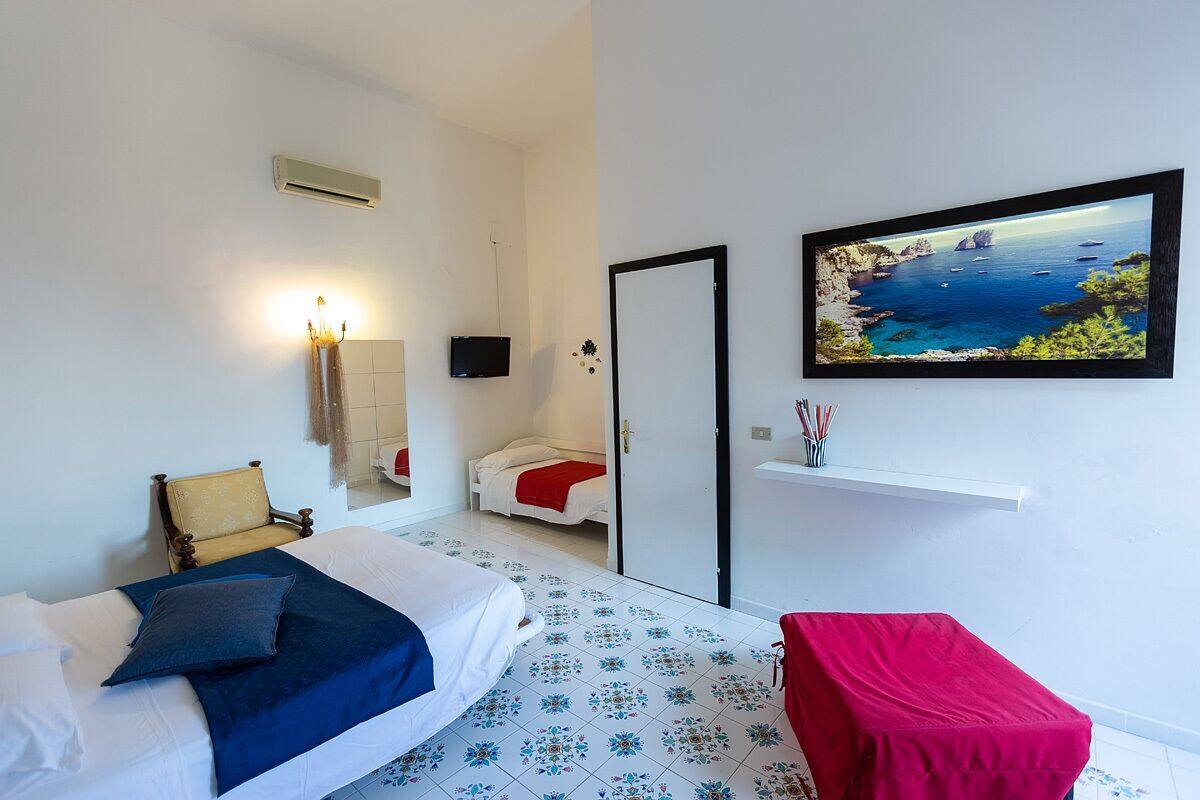 A bedroom with a bed, a chair, a TV, a door, and a wall-mounted picture of a coastal scene.
