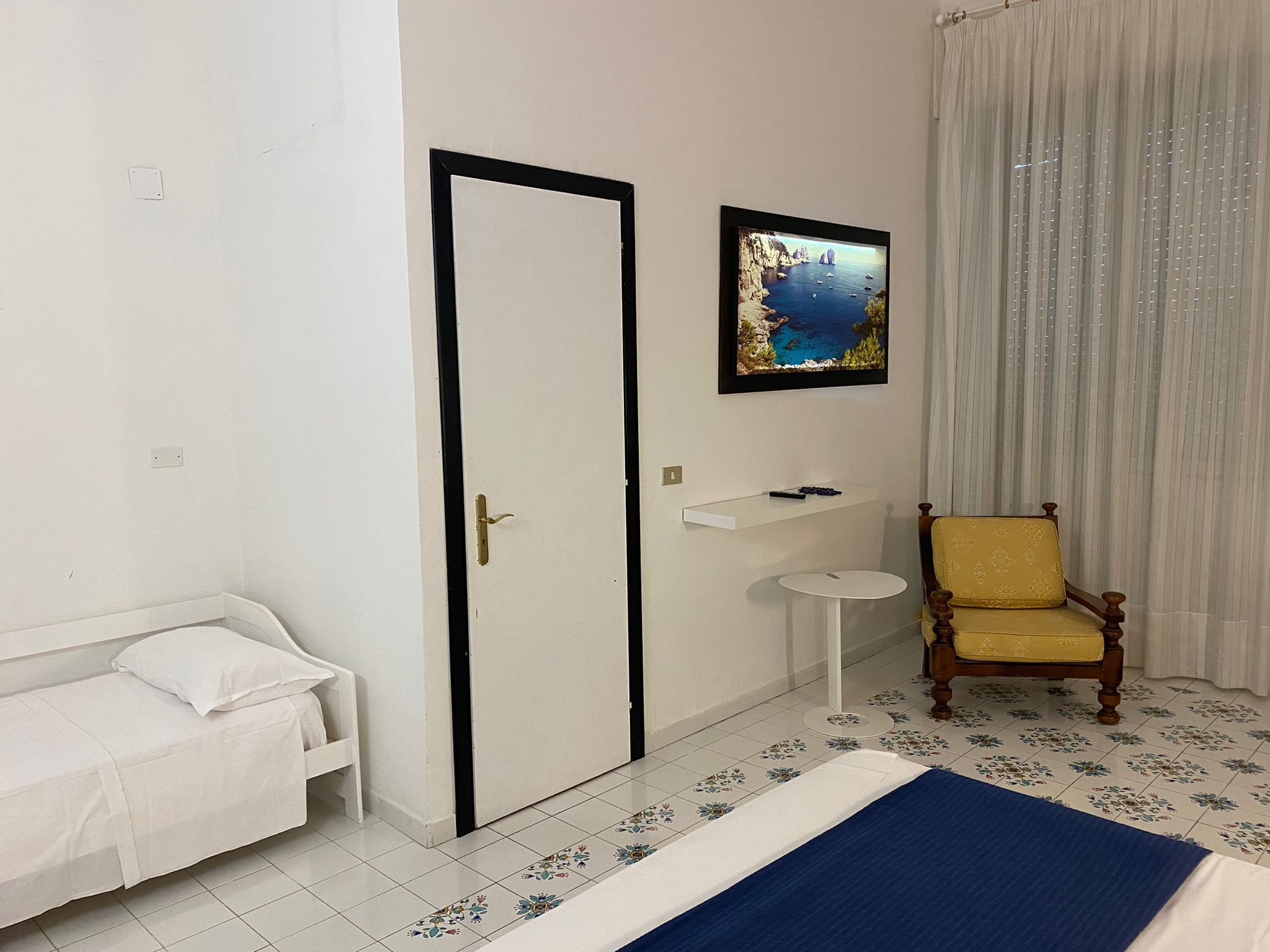 A bedroom with a bed, a chair, a small table, a framed picture, and a door.