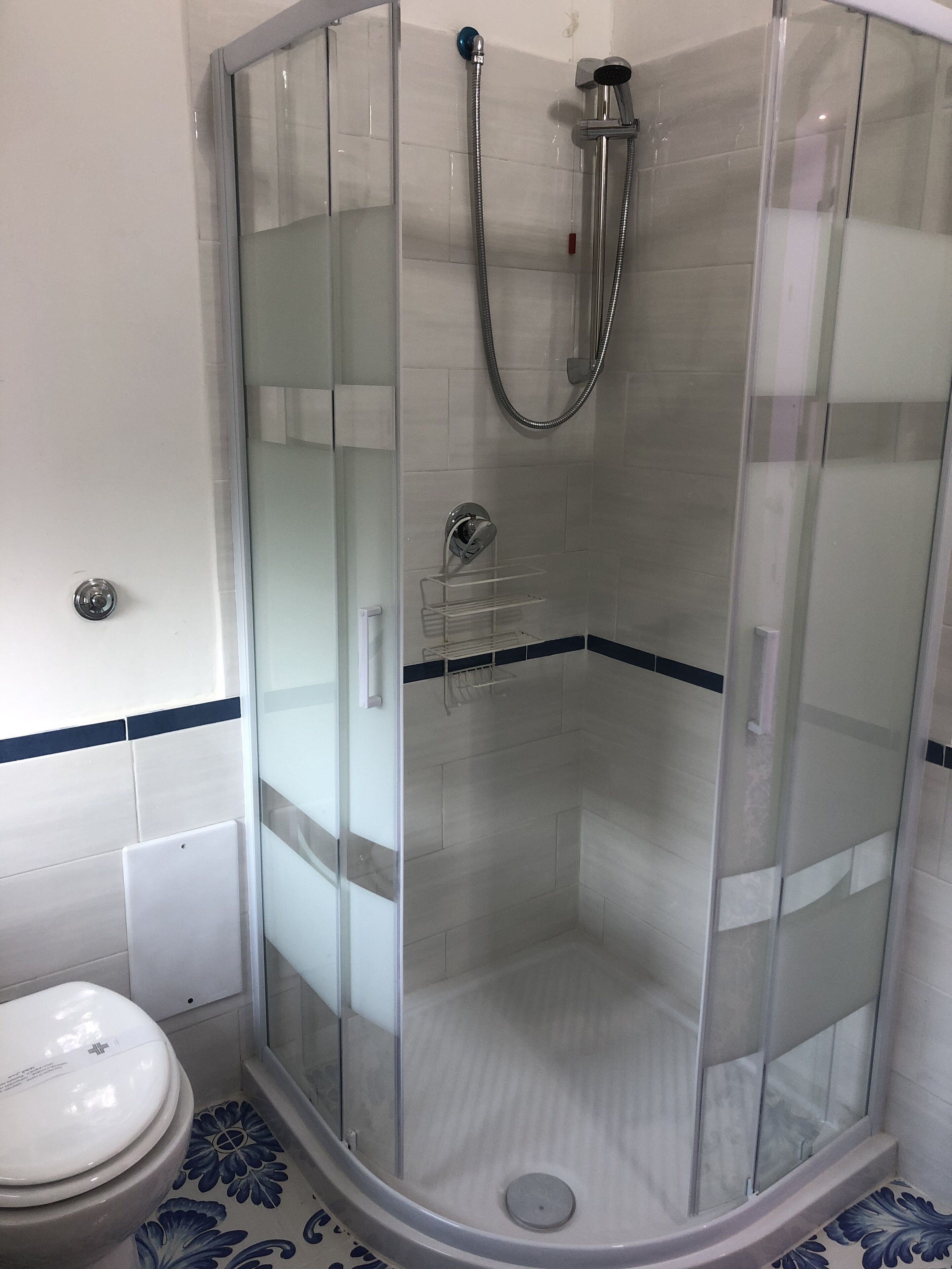 Eine begehbare Dusche mit Glaswänden, einer Handbrause und einem am Wand montierten Wasserhahn.