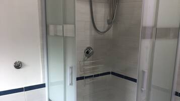 Eine begehbare Dusche mit Glaswänden, einer Handbrause und einem am Wand montierten Wasserhahn.