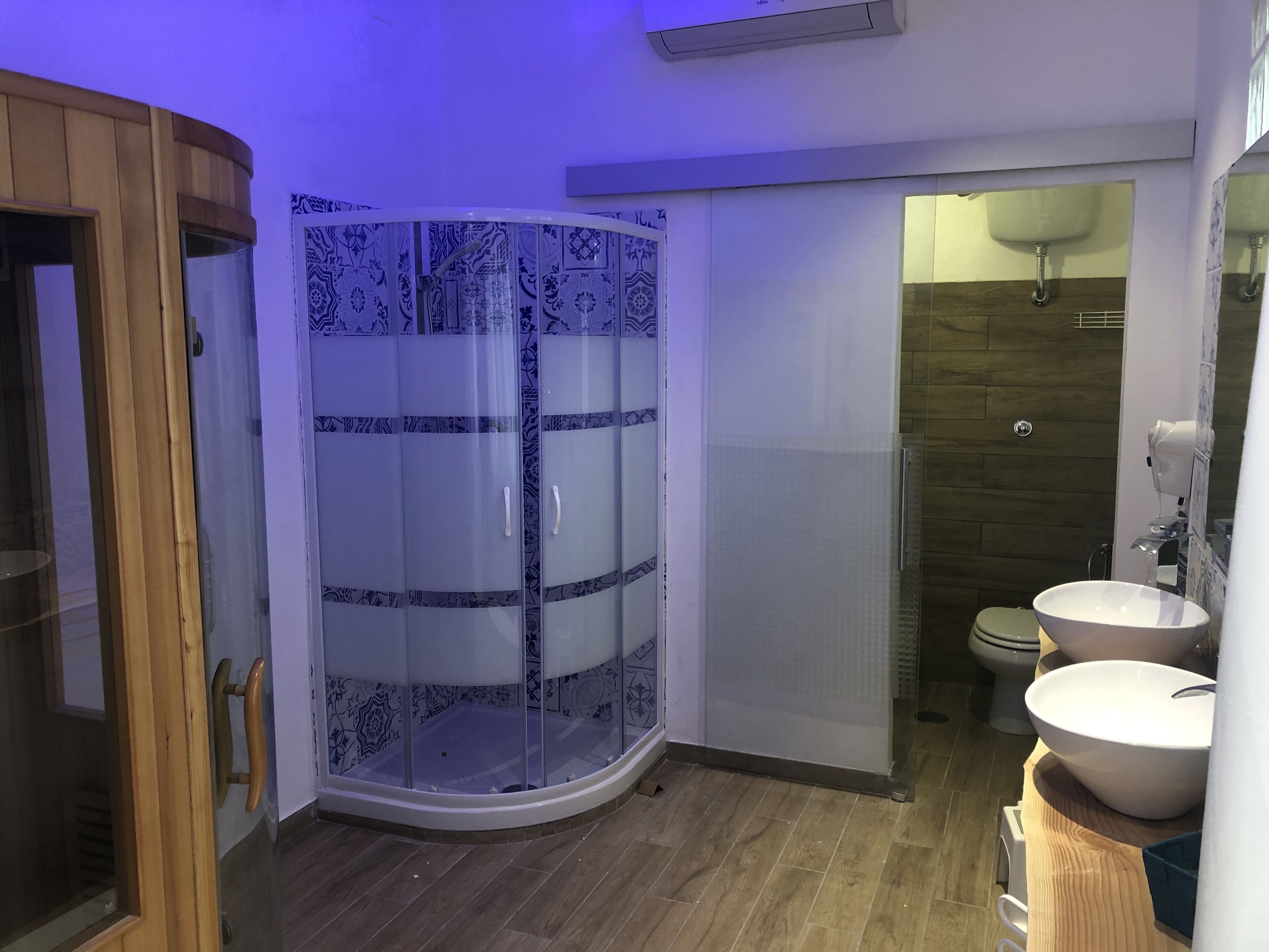 Un baño moderno con ducha acristalada, suelo de madera y dos lavamanos.