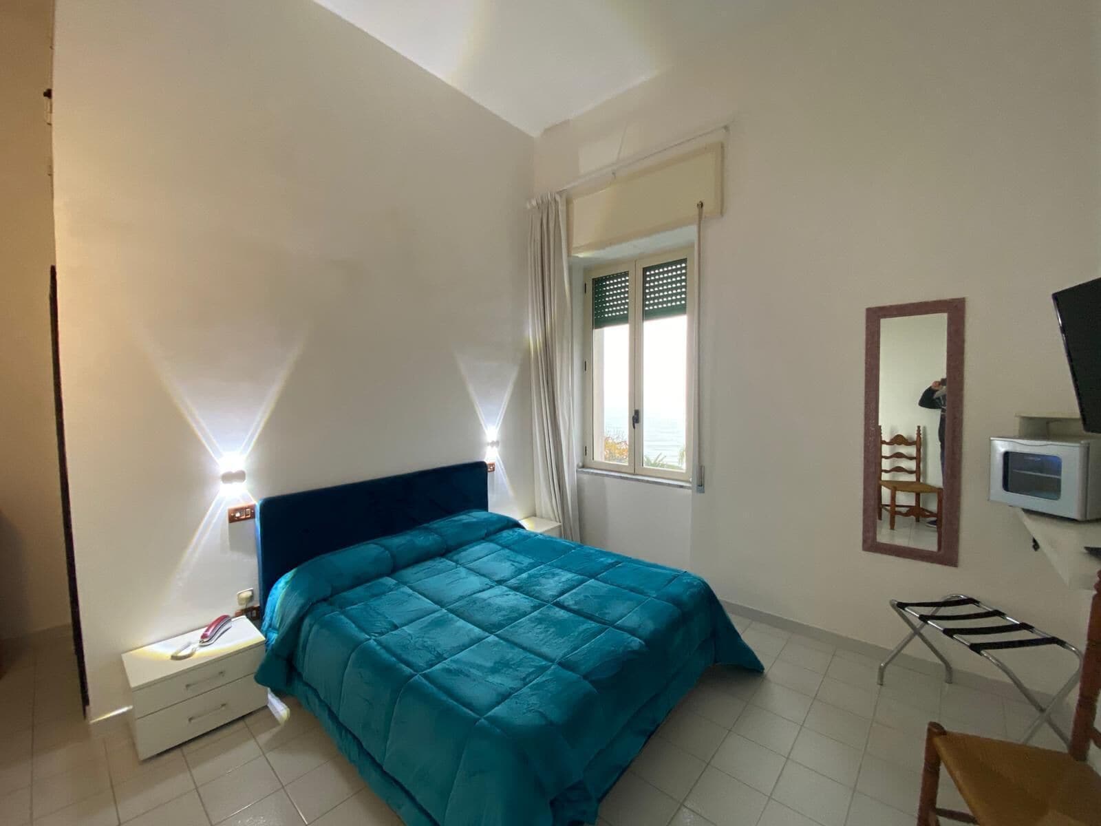 Un dormitorio con cama, mesita de noche, silla, televisor y ventana con cortinas.