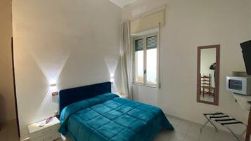 Un dormitorio con cama, mesita de noche, silla, televisor y ventana con cortinas.