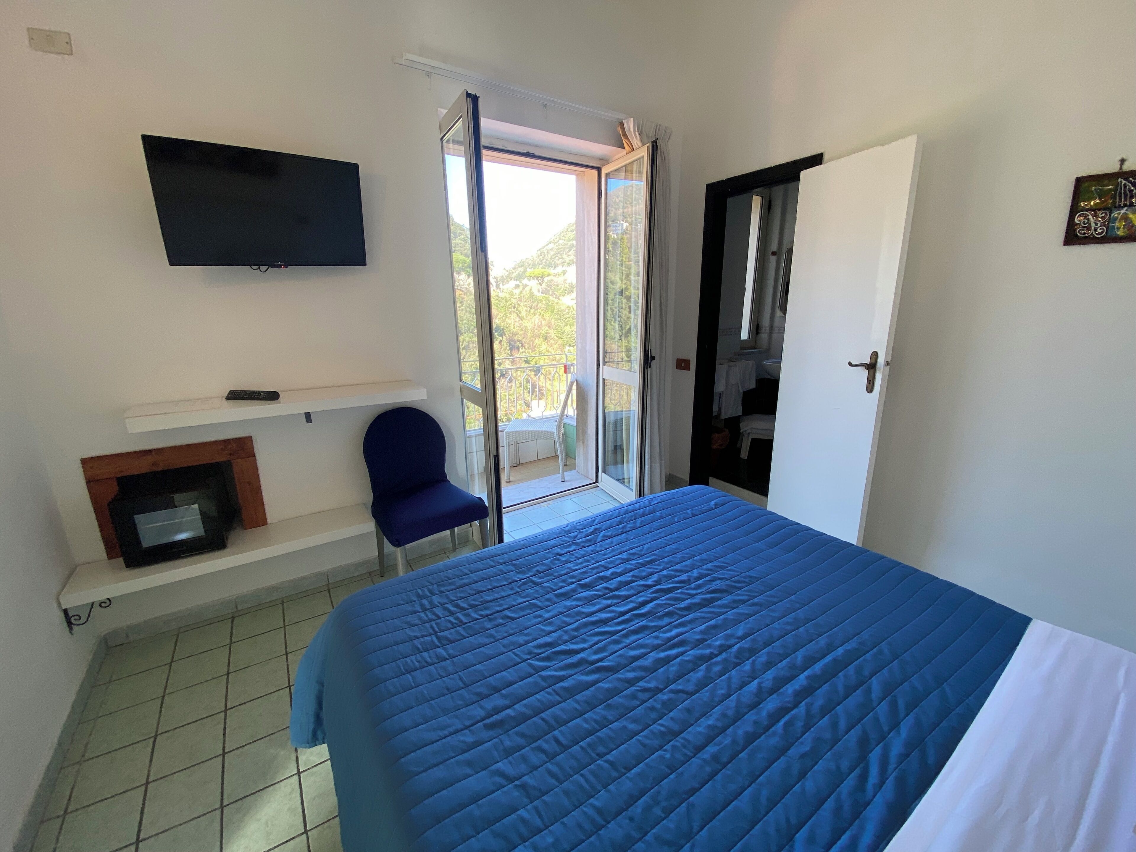 Ein Schlafzimmer mit Bett, einem an der Wand montierten Fernseher, einem Sessel, einem Kamin und einer Glastür zum Außenbereich.