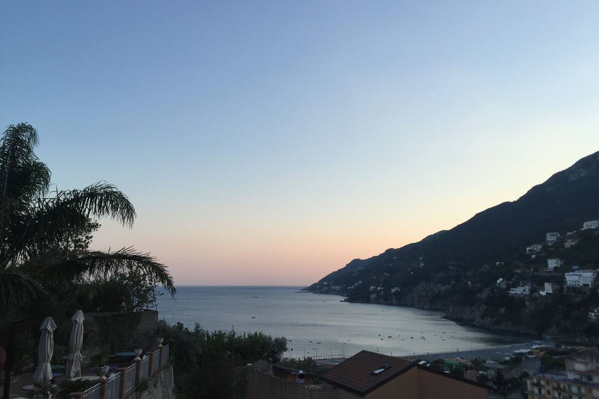 A coastal view with a clear sky, calm sea, and buildings on a hillside.