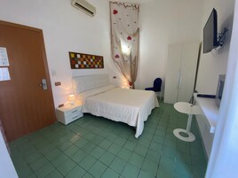 A bedroom with a bed, a nightstand, a chair, a desk, a television, and a wall-mounted air conditioner.
